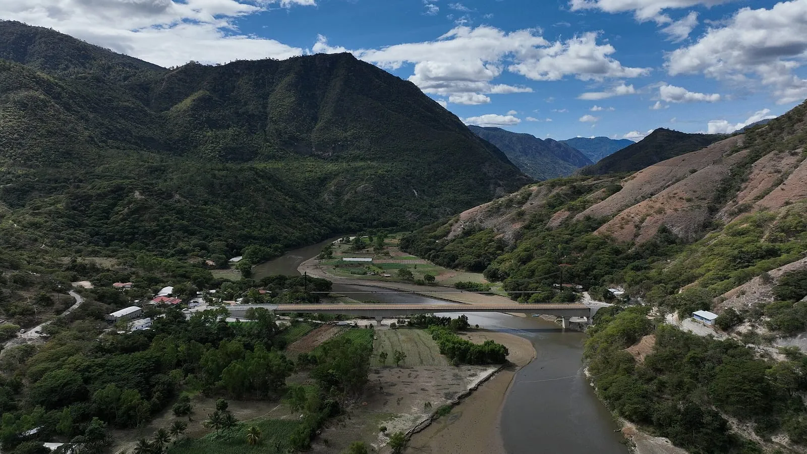 Valle verde con un río que serpentea entre montañas bajo un cielo azul con nubes
