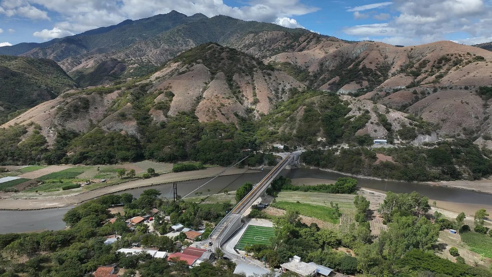 Vista aérea de montañas con laderas secas y verdes, un río y un pequeño poblado